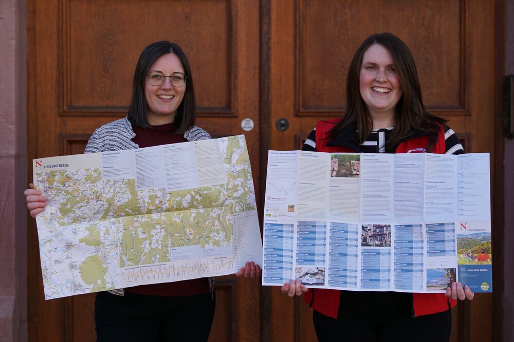 Janina Jüstl und Julia Höfle stehen vor der Tourist-Information und zeigen die neue Faltkarte
