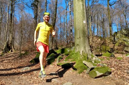 Florian Wolf in Aktion. Er trainiert an einem sonnigen Tag und läuft an einem Baum mit Nibelungensteig-Wegmarkierung vorbei.