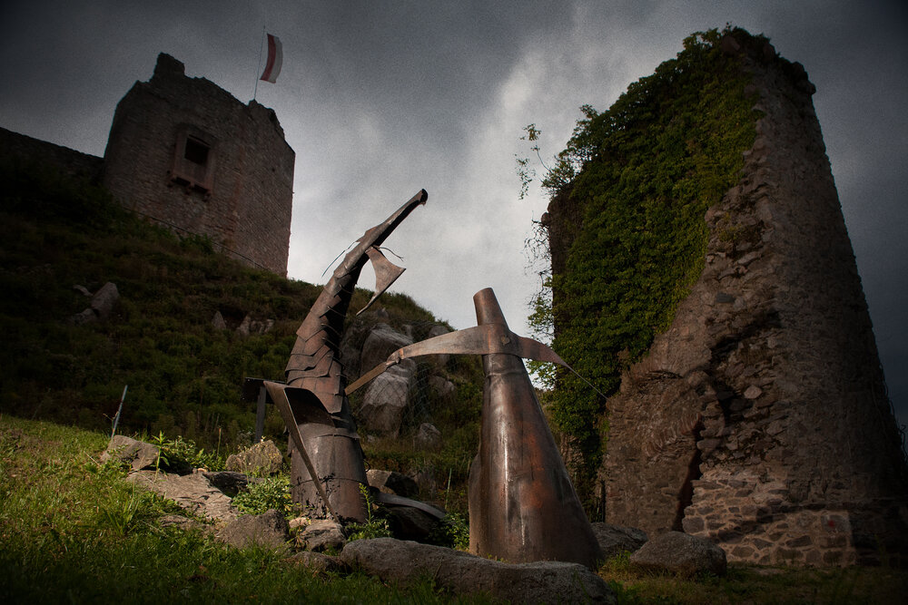 Zwei Skulpturen, die Szene aus der Nibelungensage darstellen, in der Siegfried den Drachen tötet. Im Hintergrund die Burg Lindenfels.